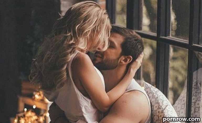 Royal Cams Sex: A Very Safe Space for Private Fantasies Couple kissing closely, embracing each other by a window indoors.